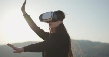 Gelecek şu andır. VR konsepti. Fütürist VR kulaklık takan bir kadın. Kadın dışarıda sanal gerçeklik gözlüğü kullanıyor. VR kulaklı kız macera oyunu oynuyor, gençlik eğlencesi, boş zaman aktivitesi