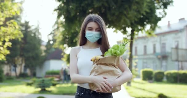 Entrega de alimentos Mujer joven en máscara protectora lleva bolsa con productos de la tienda. pandemia de Coronavirus. Entrega de alimentos en cuarentena — Vídeo de stock