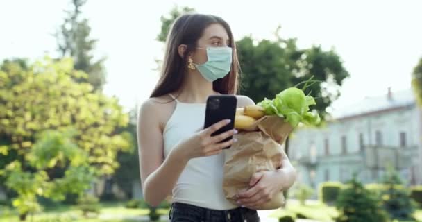 Mujer con mascarillas en la prevención del coronavirus durante la cuarentena. Entrega de comida. Mujer usando el teléfono móvil . — Vídeos de Stock