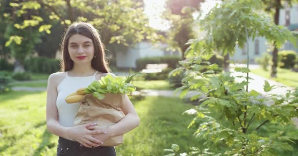 公園の緑の背景に隔離された紙のショッピングバッグを保持する若い女性のお店。販売・ショッピングの概念. — ストック動画