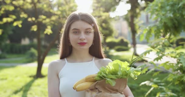 Dziewczyna używa torby wielokrotnego użytku dla świeżych owoców i warzyw. Żadnego plastikowego życia. Ekologiczna torba. Portret atrakcyjna kobieta trzyma torbę z papieru spożywczego mając dobry nastrój i uśmiecha się. — Wideo stockowe