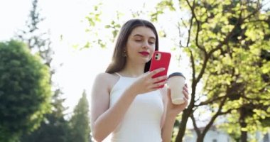 Cep telefonunda mesajlar yazan çekici kız. Parkta elinde akıllı telefon ve fincan kahveyle duran Pretty Woman 'ın portresi. Çevrimiçi konuşmasında mesajlar yazarken aranıyor