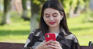 Müzikten hoşlanan ve parkta mesaj yazan bir kadın. Müzik dinleyen neşeli genç bir kadın kulaklık takıyor Kafkasya 'nın arka planındaki akıllı telefon gülüşüne bakıyor.