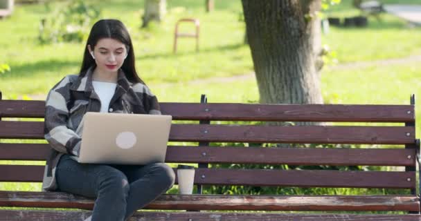 若い学生はオンラインレッスンを見て、公園から勉強します。ラップトップコンピュータを使用して女子大生。パソコン技術で学ぶオンライン教育の概念. — ストック動画