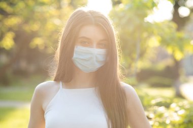 Yüzünde koruyucu bir tıbbi maske takmış beyaz bir esmerin yakın portresi. Grip virüsü ve koronavirüs salgını her yerde..