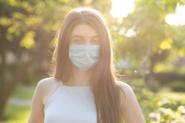 Yüzünde koruyucu bir tıbbi maske takmış beyaz bir esmerin yakın portresi. Grip virüsü ve koronavirüs salgını her yerde..