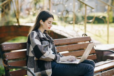 İnternetten ders izleyen ve parkta ders çalışan genç bir öğrenci. Dizüstü bilgisayar kullanan bir üniversite öğrencisi. Bilgisayar teknolojisi online eğitim konseptiyle çalışma.