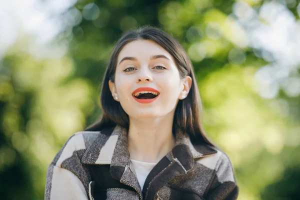 Ritratto ravvicinato di bella ragazza con lunghi capelli ricci su strada su sfondo alberi neri. labbra rosse e sorridente alla macchina fotografica — Foto Stock
