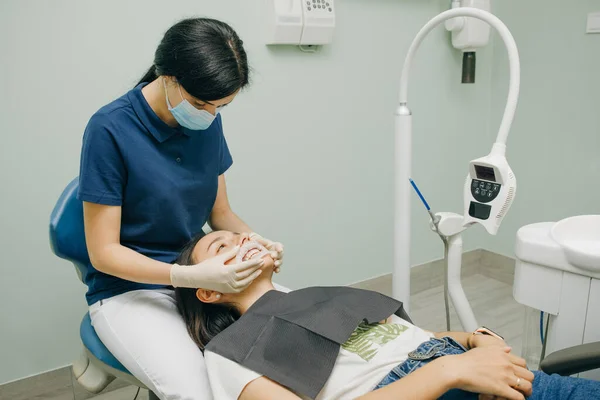 Dentista feminina em luvas de látex branco médico coloca represa de borracha em um paciente em uma clínica odontológica. Limpar dentes. Escritório odontológico moderno — Fotografia de Stock