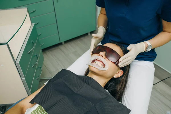 Cliente feminina de uma clínica senta-se com a boca aberta em uma cadeira dentária, usando óculos de segurança laranja. Escritório dentário. Odontologia. Estomatologia — Fotografia de Stock