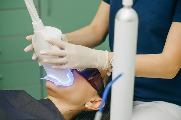 Procedimento de clareamento dos dentes. Dentista estomatologista clareamento dos dentes para o paciente na clínica odontológica medicina com lâmpada. Fonte de luz poderosa é direcionada para a boca do paciente para acelerar o processo . — Fotografia de Stock