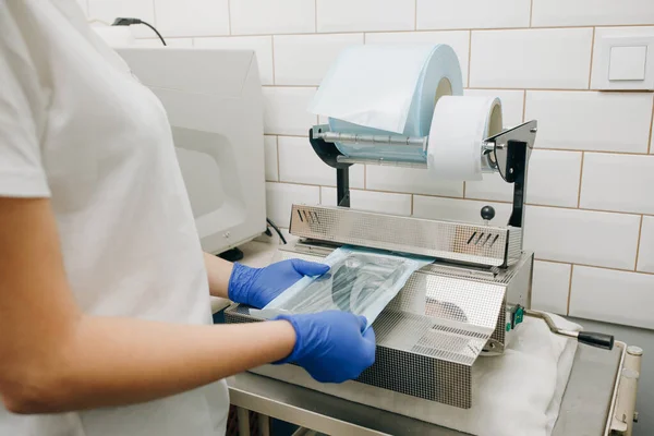 Zahnarzthelferhände in Handschuhen verpacken zahnärztliches Instrumentarium-Set zum Autoklavieren in einer Plastiktüte mit Vakuumverpackungsmaschine. Sterilitäts- und Sicherheitskonzept. — Stockfoto