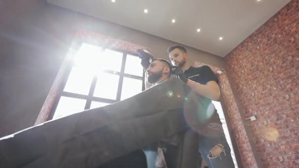 Kapper maken kapsel met elektrische trimmer in mannelijke salon. Kapper met donker haar met zwarte handschoenen die een knipbeurt doet voor de klant in de kapperszaak. Stylist met trimmer en haarborstel. — Stockvideo