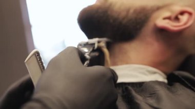 Berber dükkanında sakallı adamı tıraş eden berber. Erkek cilt bakımı ve sakal stili konsept. Siyah eldivenli profesyonel bir kuaför saç kesimi yapıyor..