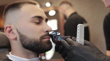 Saç şekillendirme işlemi. Genç sakallı bir adamın saçını kurutan berber. Saç kesimi. Erkekler umursar. Sakallı, vahşi bir adam. Kuru tıraş. Elektrikli tıraş makinesi.