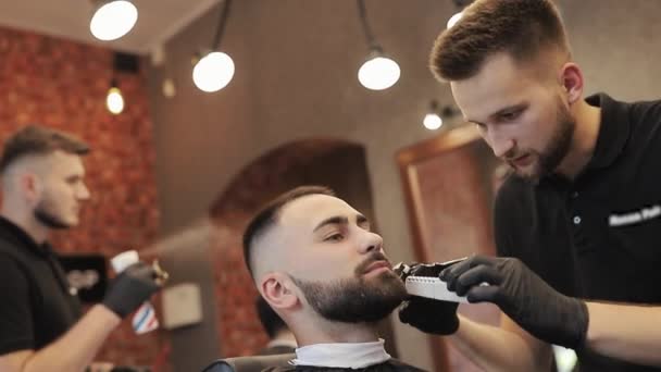 Barber holder barberkniv i hænder og barberer ansigtet af mennesket. Mandlig frisør iført sorte handsker, mens du arbejder i salon. Skægget voksen mand sidder på moderne barbershop. – Stock-video