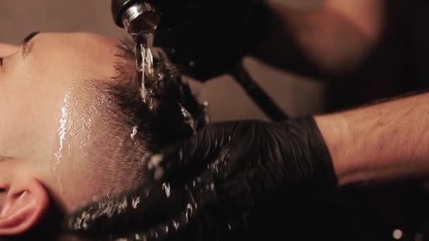 Κομμωτής χέρι πλύσιμο του αφρού σαμπουάν από αρσενικά μαλλιά με νερό στο σαλόνι αρσενικό. Πλύνετε το κεφάλι και τα μαλλιά των ανδρών με στο κουρείο. Ανδρική φροντίδα μαλλιών έννοια — Αρχείο Βίντεο
