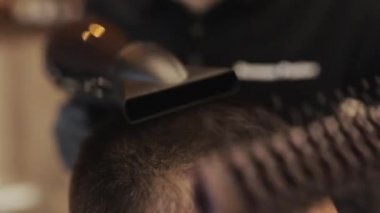 Kuaför, erkek kuaföründe saç stili yapıyor. Siyah eldivenli, siyah saçlı berber berber dükkanında müşterisinin saçını kesiyor.