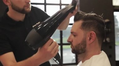 Profesyonel ve düzgün saç bakımı. Saç ve sakal kesiyorum. Kuaför, erkek kuaföründe saç stili yapıyor. Siyah eldivenli, siyah saçlı berber berber dükkanında müşterisinin saçını kesiyor.