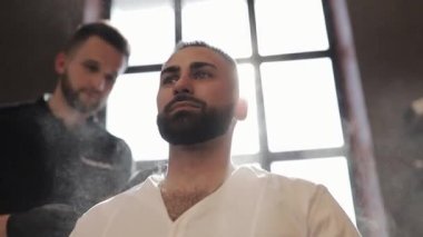 Berber tıraş olduktan ve saç kestikten sonra erkek yüzünü süpürüyor. Profesyonel berber, berber dükkanında saç ve sakal kesiminden sonra müşterilerine cilt bakım ürünü uygular. Profesyonel saç tedavisi.