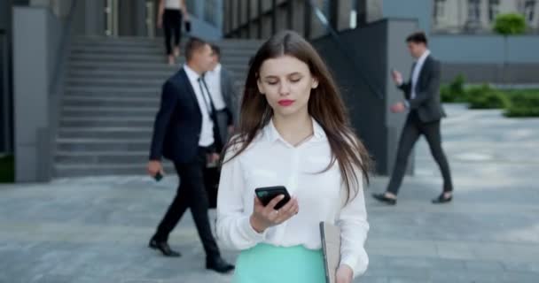 Stijlvolle zakenvrouw die haar telefoon buiten gebruikt. Mooie vrouw met lang haar lezen van een bericht met behulp van haar smartphone in de voorkant van het gebouw — Stockvideo