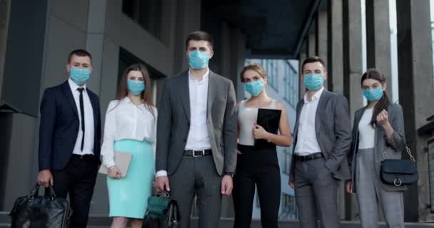Retrato del equipo corporativo en máscara protectora. Gente de negocios profesional en máscara protectora mira la cámara de pie fuera del centro de negocios — Vídeos de Stock