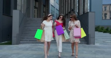 Ellerinde renkli çantalarla binadan çıkan bir grup mutlu genç kadın. Güneşli Gün, Başarılı Alışveriş.