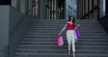 Giysileriyle merdivenlerden elinde poşetlerle inen genç ve güzel bir kız..