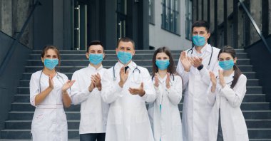 Corona Virüsü ve Sağlık Hizmetleri Konsepti. Coronavirus 'la savaşan hastane personeli destekleri için halkı alkışlıyor. Yüz maskeli bir grup doktor kameraya bakıyor..