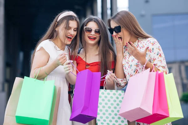 Başarılı bir alışveriş. Günlük makyaj. Ellerinde sarı, yeşil, mor ve pembe çantalarla binadan çıkan sıradan elbiseli ve pantolonlu bir grup mutlu genç kadın. — Stok fotoğraf