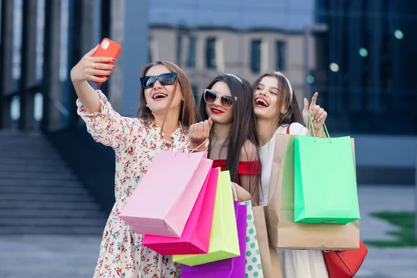 Güneş gözlüğü, makyaj, saç halkası ve renkli alışveriş torbalarıyla başarılı bir alışveriş sonrası selfie çeken bir grup genç kız. — Stok fotoğraf