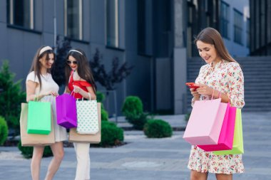 Arka planda bir grup arkadaşı olan mutlu bir alışveriş kadını. Perakende satış, jest ve satış konsepti. Alışveriş merkezindeki alışveriş torbalarıyla gülümseyen genç kız.