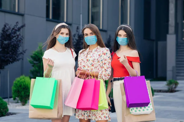 A fiatal nők maszkot viselnek, hogy megvédjék a koronavírus világjárványt színes táskákkal a kezükben. Fogyasztóvédelem, vásárlás, vásárlás, életmód koncepció. — Stock Fotó