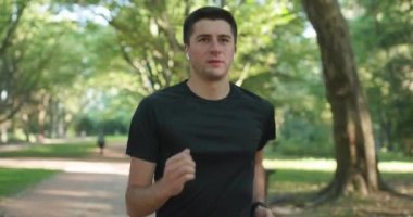 Şehir parkında bluetooth kulaklık ve akıllı saat uygulaması kullanarak koşan yetişkin bir adam sağlıklı aktif yaşam tarzının keyfini çıkarıyor. Erkek koşucu kardiyo egzersizi yapıyor..