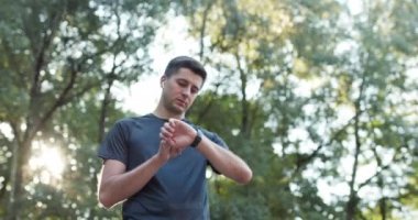 Yetişkin adam akıllı saat kullanıyor dokunmatik ekran kullanıyor sağlıklı aktif yaşam tarzının tadını çıkarıyor. Erkek koşucu yaz parkında kardiyo egzersizi yapıyor. Taşınabilir modern kulaklıklar