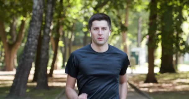 Férfi nyári sport egyenruhában fut a városi parkban okosórával méri a sebességet, a távolságot és a pulzusszámot. Vezeték nélküli fülhallgató. Kiképzés odakint. 4K RAW