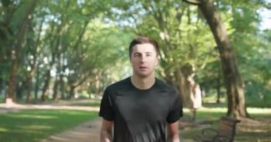 Şehir parkında bluetooth kulaklık ve akıllı saat uygulaması kullanarak koşan sporcu sağlıklı aktif yaşam tarzının keyfini çıkarıyor. Erkek koşucu yaz güneşinde kardiyo egzersizi yapıyor..