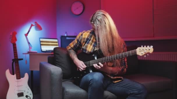 L'homme joue de la guitare électrique. Heavy metal ou rock. Guitariste virtuose jouant une guitare électrique sur canapé avec lumières LED couleur At Home Studio — Video