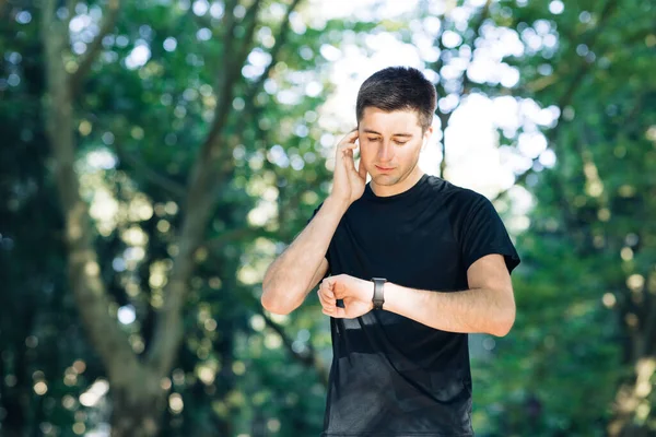 Hombre adulto corriendo al aire libre usando auriculares inalámbricos escuchando música con smartwatch disfrutando saludable. Corredor masculino haciendo ejercicio cardiovascular en el parque de la ciudad — Foto de Stock