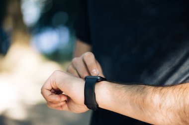 Siyah dokunmatik ekranın dışındaki modern akıllı saat cihazıyla erkek eli görüntüsünü kapat. Online bildirimi kontrol ediyorum. Mesafe ölçümü, kalp atışı. Sağlık Hizmetleri