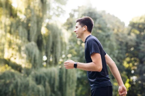 Hombre guapo usando auriculares de moda y reloj inteligente. Entrenamiento de deportistas fuera disfrutando de la naturaleza fresca. Vida activa saludable. Día soleado de verano. Distancia, aplicación deporte latidos del corazón — Foto de Stock