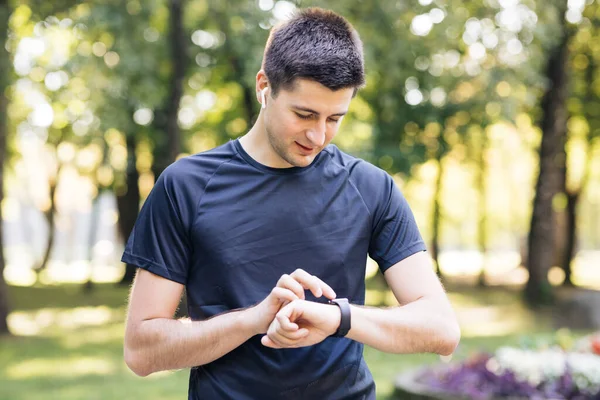 Yetişkin adam akıllı saat kullanıyor dokunmatik ekran kullanıyor sağlıklı aktif yaşam tarzının tadını çıkarıyor. Erkek koşucu yaz parkında kardiyo egzersizi yapıyor. Taşınabilir modern kulaklıklar — Stok fotoğraf