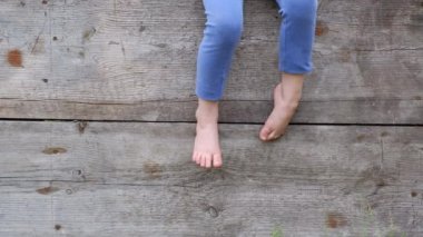 Ahşap bir çit oturan bir küçük köylü çocuğun çıplak ayak takılmak
