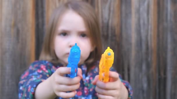 Verängstigtes kleines verschwommenes Mädchen hält eine orange-blaue Spielzeugpistole in den Händen — Stockvideo