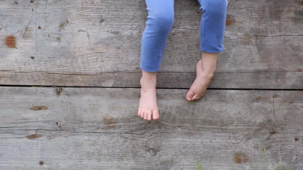 Pés nus de uma pequena criança camponesa sentada em uma cerca de madeira sair — Vídeo de Stock