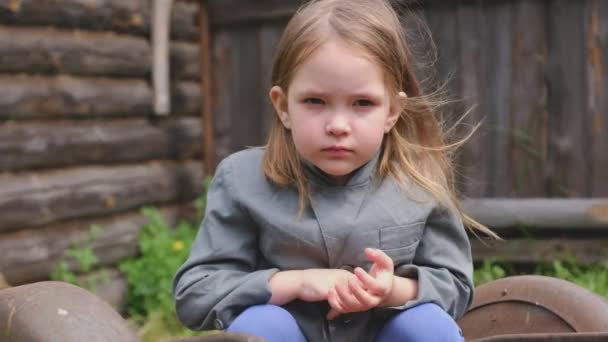 Niña linda en una chaqueta gris está sentado en un viejo carro oxidado — Vídeos de Stock