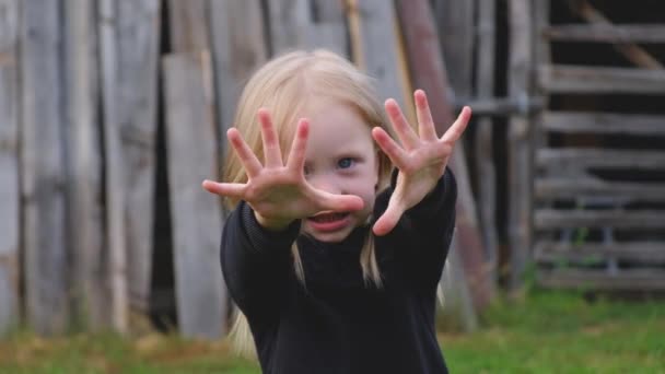 Gyönyörű kislány kék szeme egy fekete pulóver húzza a kezét felé — Stock videók