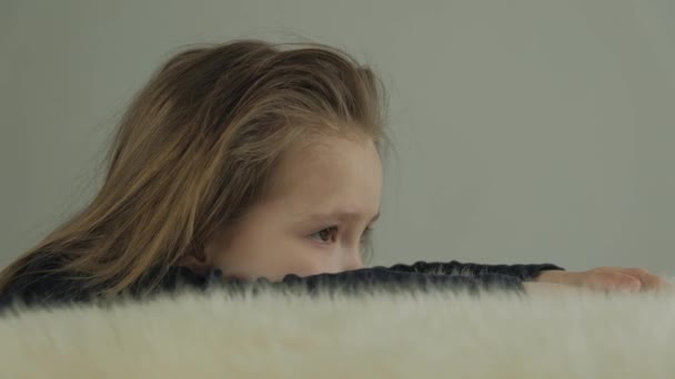 Triest klein meisje opgestapeld op een tafel met een witte schapen huid — Stockvideo