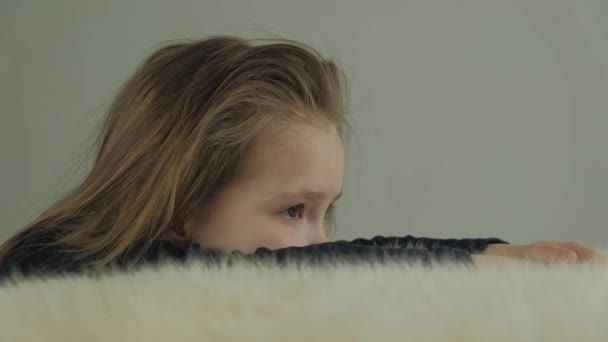 Niña triste apilada en una mesa con una piel de oveja blanca — Vídeo de stock