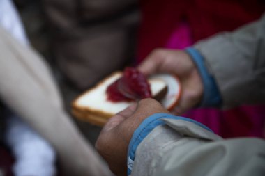 Kaşıkla bir parça ekmeğin üzerine reçel koyan bir el.